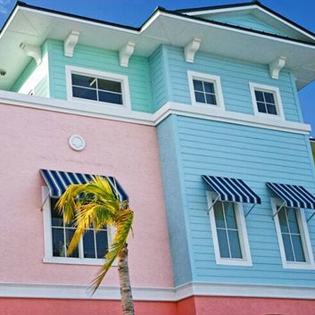 Pastel pink and blue seaside house with striped awnings and a palm tree in front