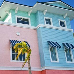Pastel pink and blue house facade with striped awnings and a palm tree in front.