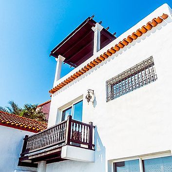 White stucco house with a small balcony, orange roof tiles, and a blue sky background
