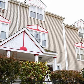 Row of beige townhouses with white trim, red accents, and shrubs in front