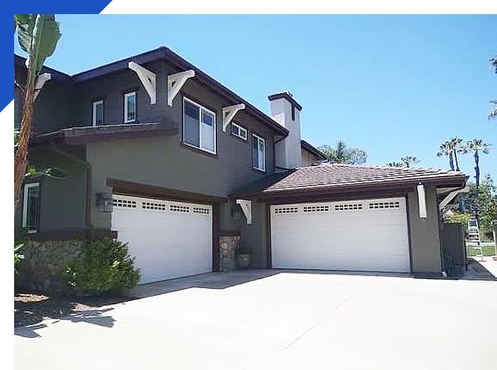 Two-story suburban house with two white garage doors and a bright driveway under a blue sky
