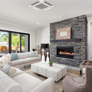 Bright living room with white sofas, stone fireplace, and a coffee table in front of large windows