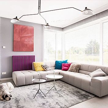 Modern living room with gray sectional sofa, colorful pillows, round tables, and large bright windows