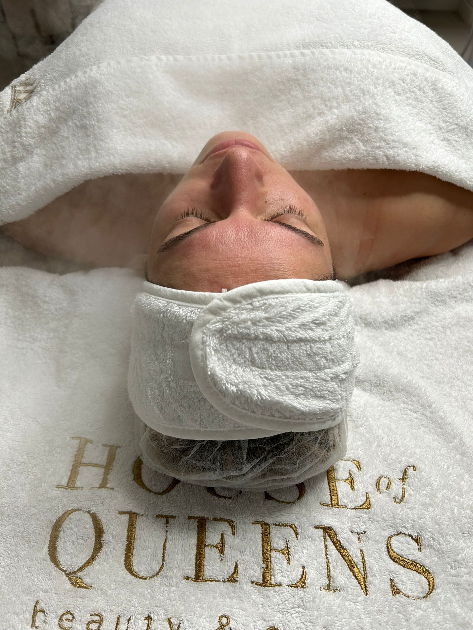 Eine Frau liegt auf einem Bett, ihr Kopf ist in ein Handtuch mit der Aufschrift „House of Queens“ gewickelt