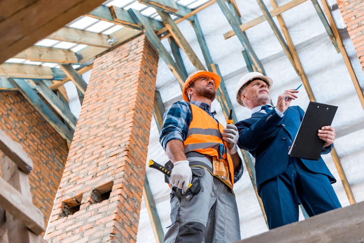 Due operai edili con l'elmetto esaminano i progetti all'interno di un edificio in mattoni in costruzione.