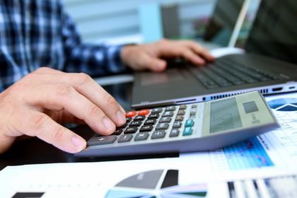 Person using calculator and laptop, working with financial documents.