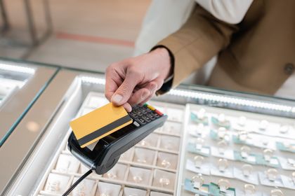 Person paying with a gold credit card at a jewelry store counter.