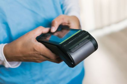 Person holding a black handheld payment terminal, tapping the screen with their fingers.