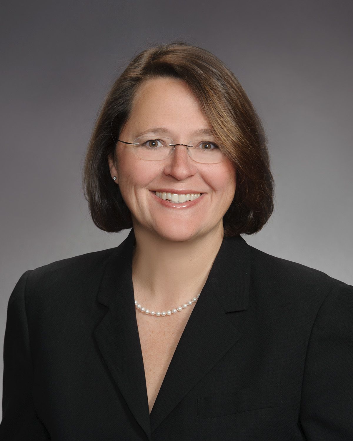 A woman wearing glasses and a pearl necklace smiles for the camera
