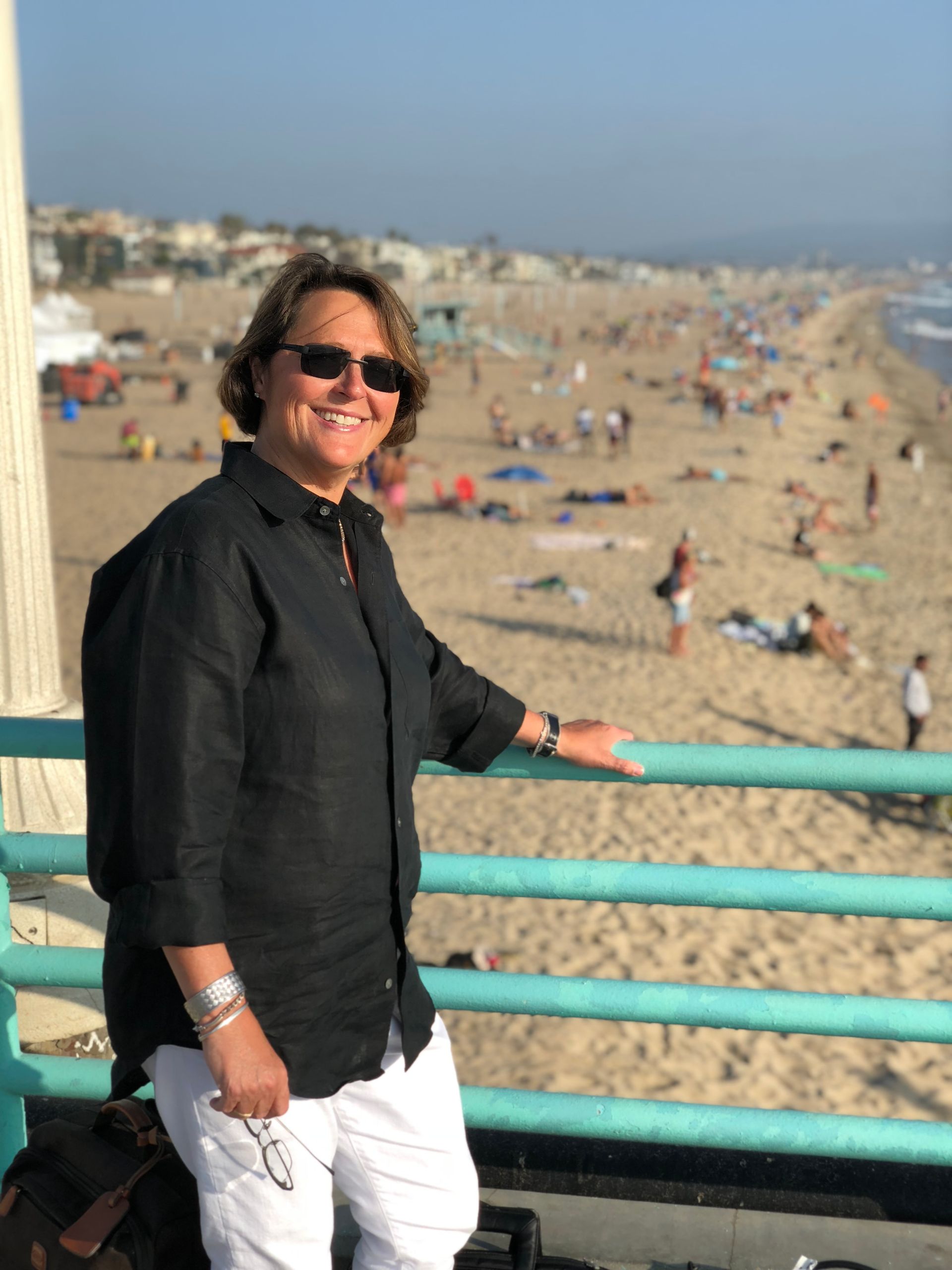 A woman is standing on a pier looking at the beach.