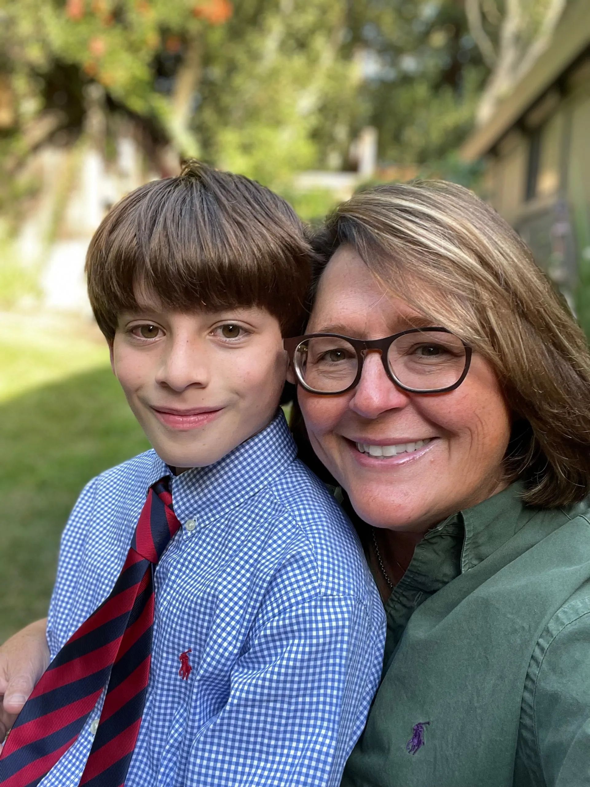 A person in a green button-down shirt smiles beside a person in a blue checkered dress shirt and red-striped tie.