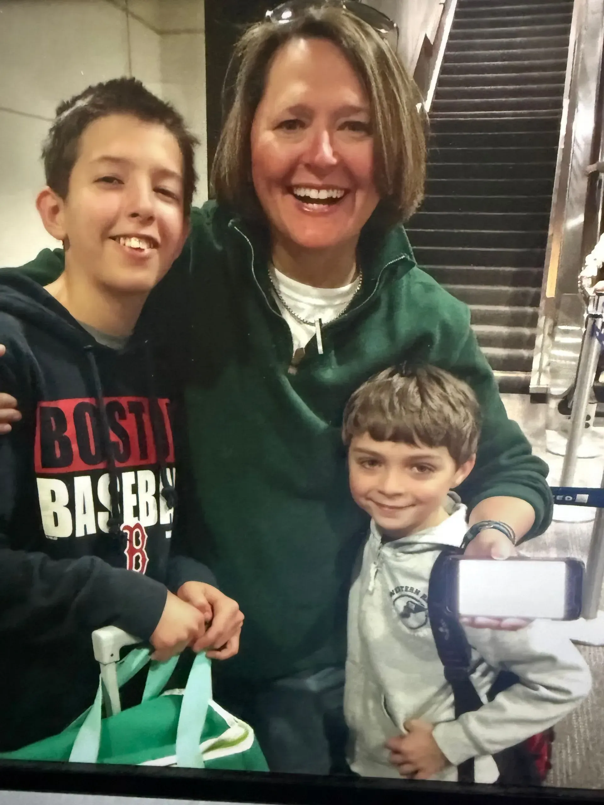A woman is posing for a picture with two children one of whom is wearing a boston baseball sweatshirt
