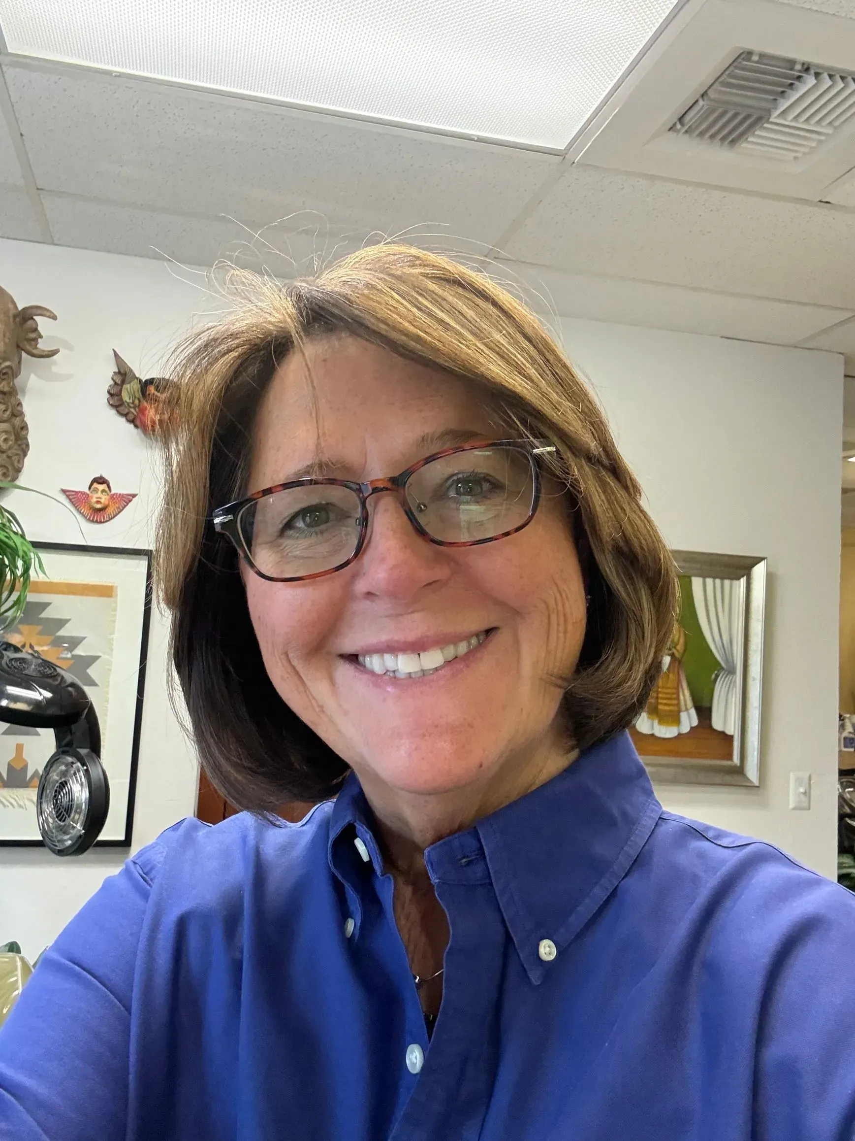 A woman wearing glasses and a blue shirt is smiling for the camera.