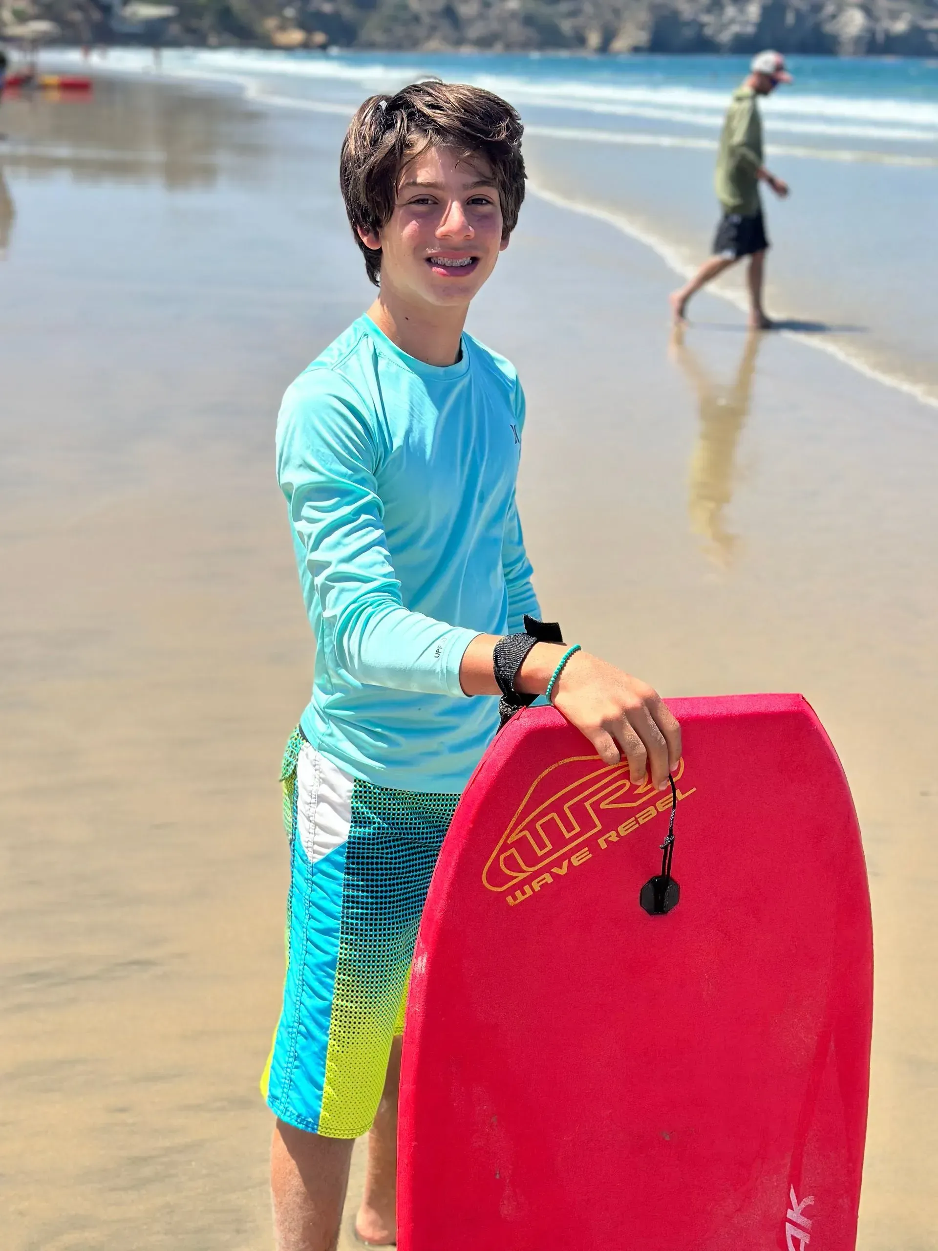 A young boy is holding a red boogie board on the beach.