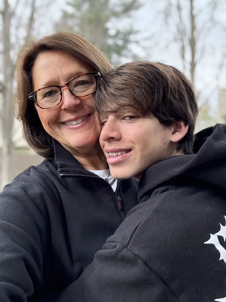 Two people smiling and hugging outdoors in black hoodies, with bare trees in the background