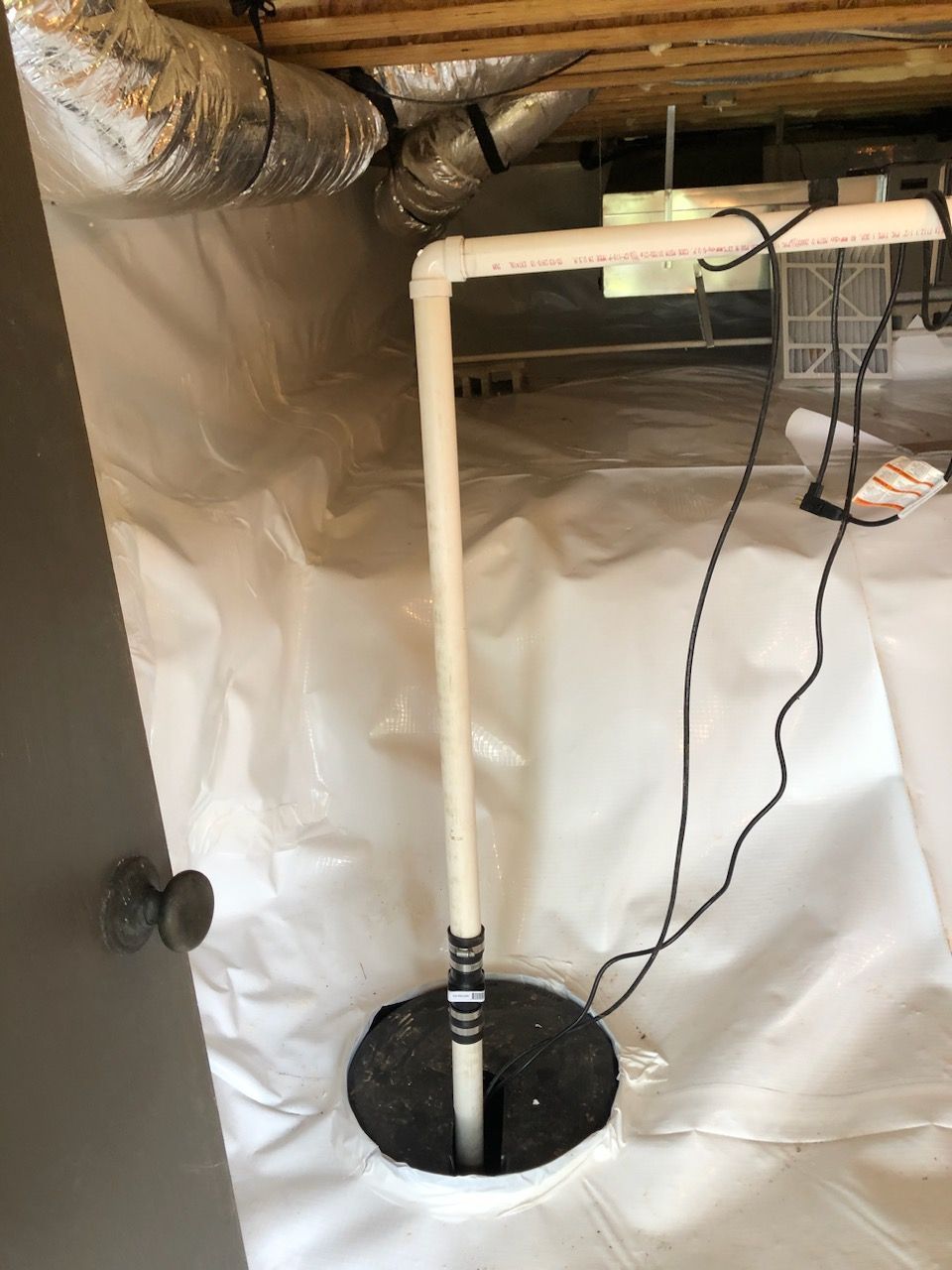 A white pipe is connected to a drain in a basement.