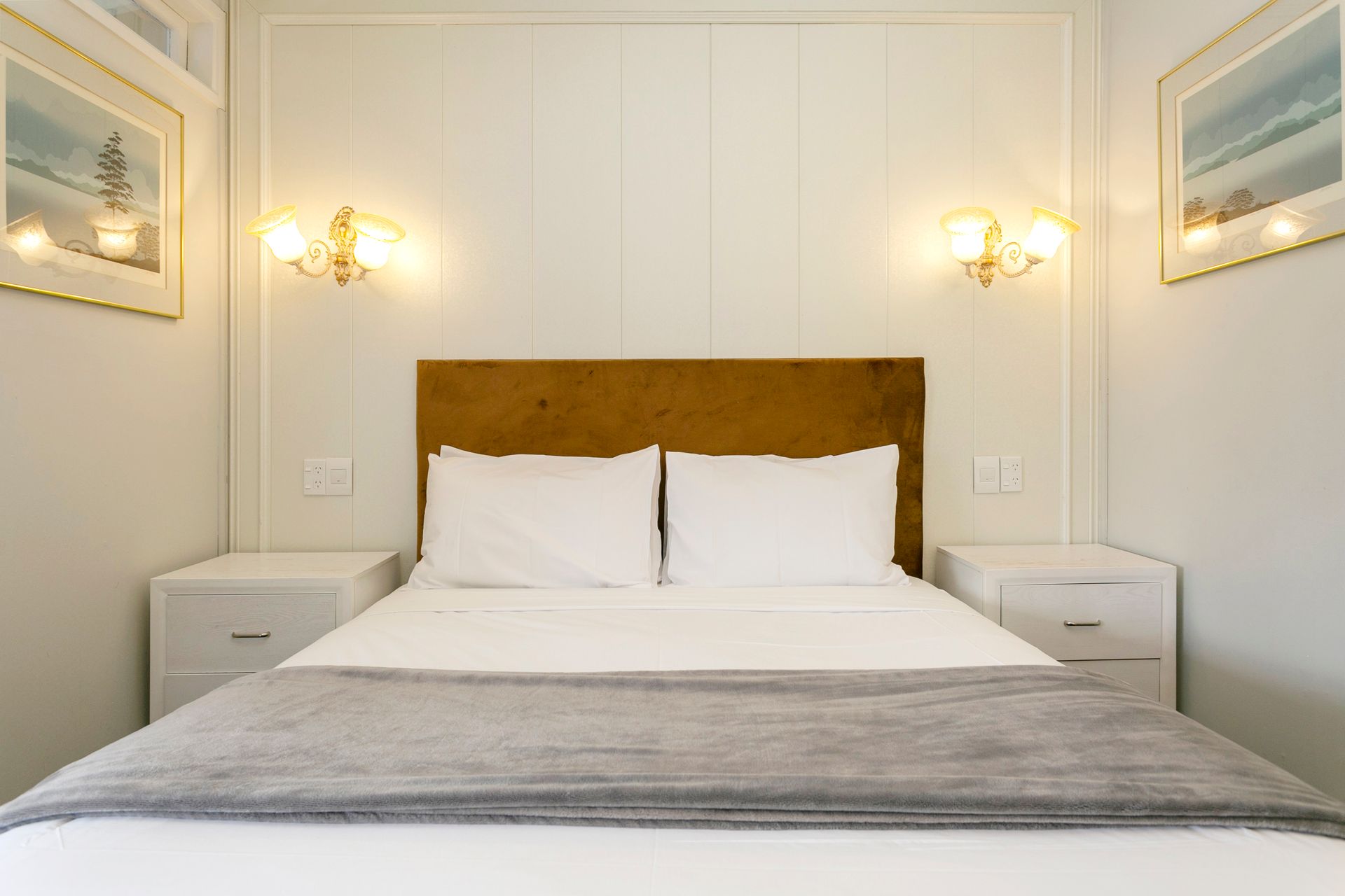 A bedroom with a bed , two nightstands and two pictures on the wall.