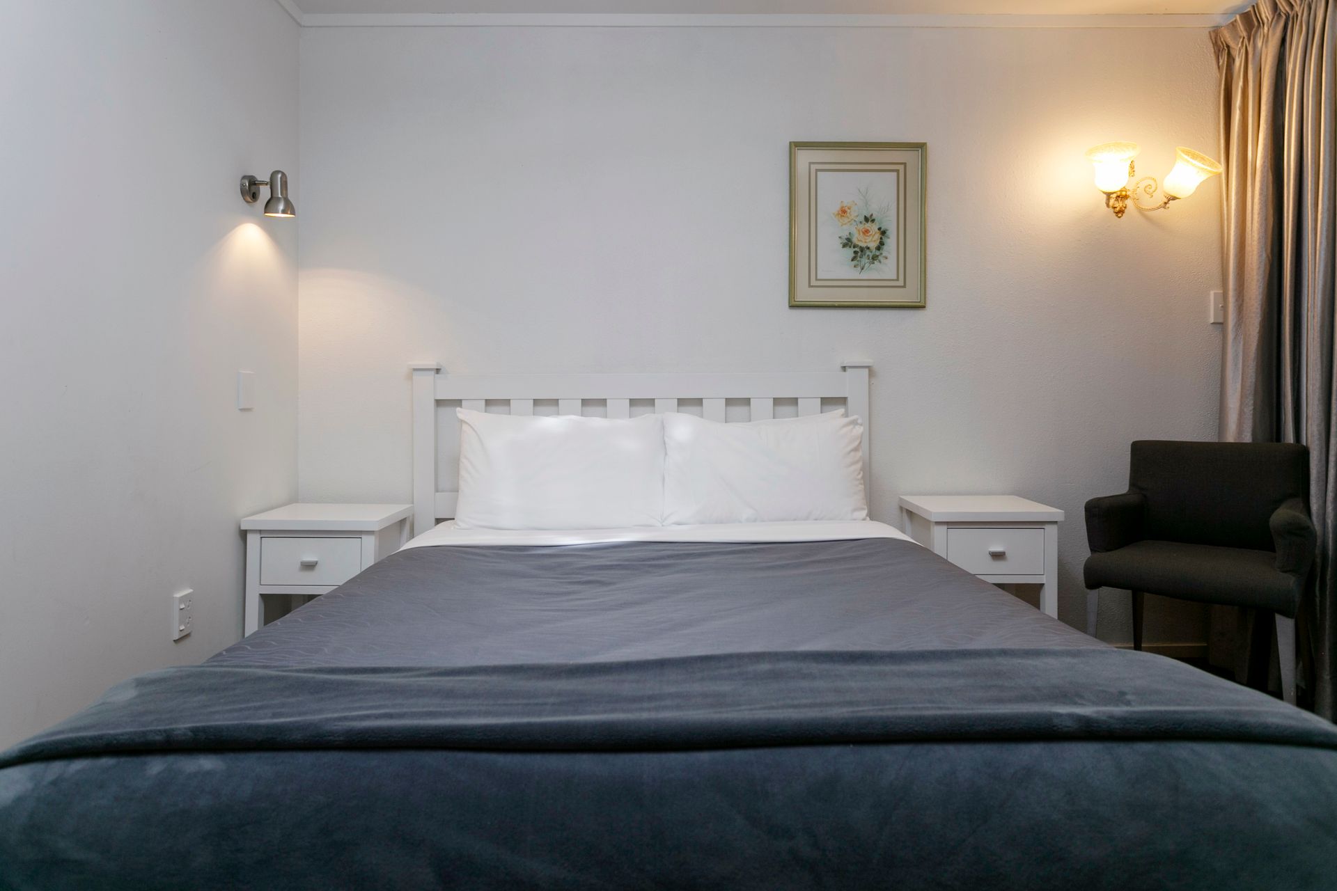 A hotel room with a bed , chair , table and nightstand.