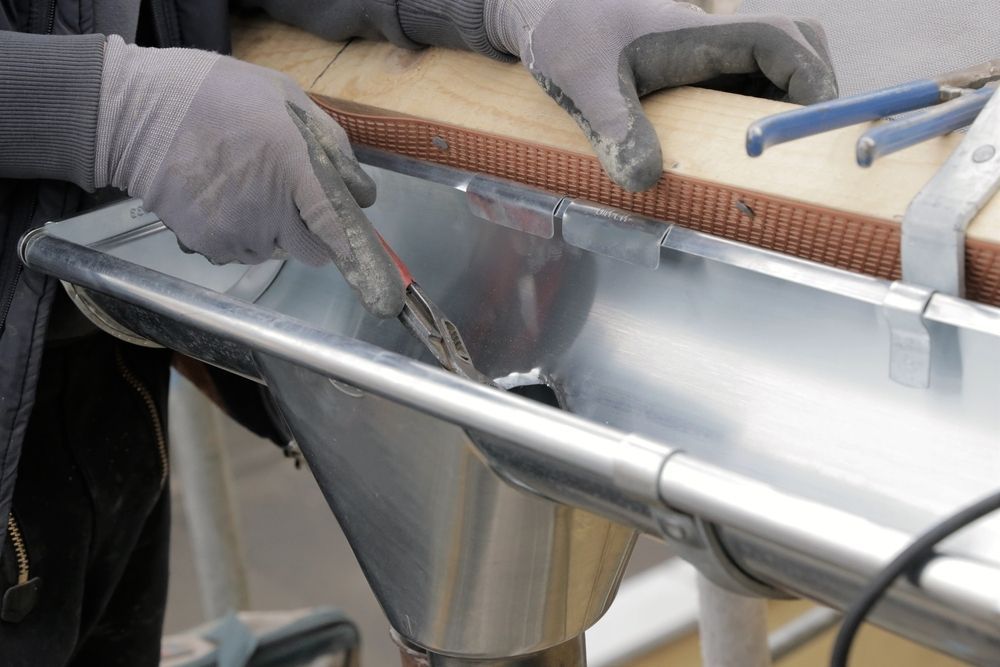 A Person is Working on a Metal Gutter With a Pair of Pliers — Bradshaw Plumbing & Roofing Pty Ltd In Marian, QLD