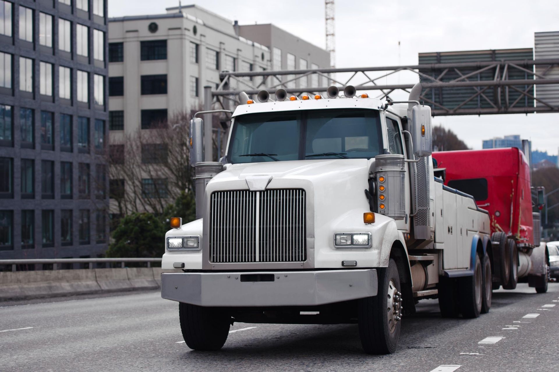 A white tow truck is driving down a highway next to a red semi truck.