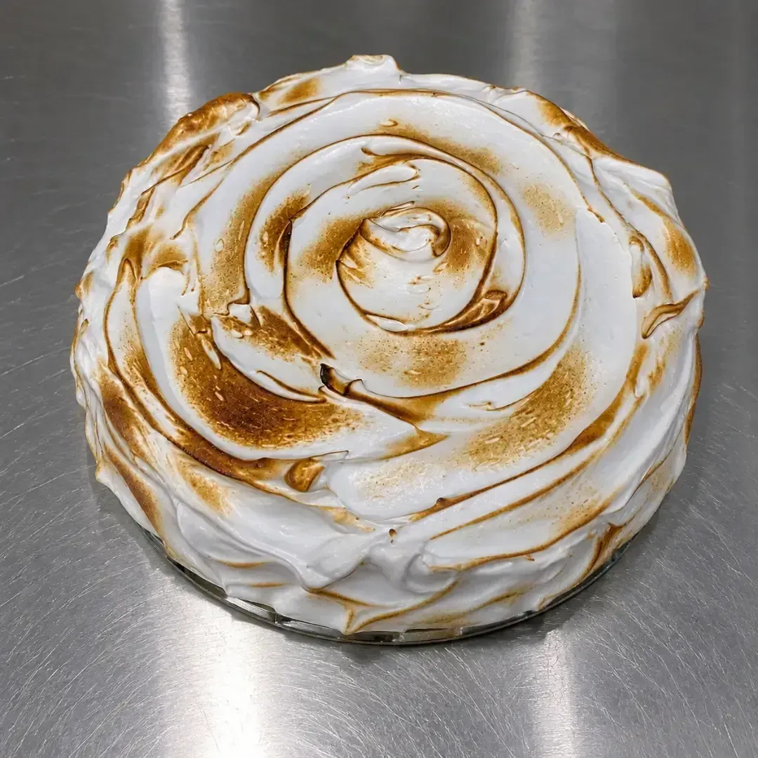 Postre blanco con forma de rosa y acabado esmerilado, con un chorrito de caramelo, sobre una superficie metálica