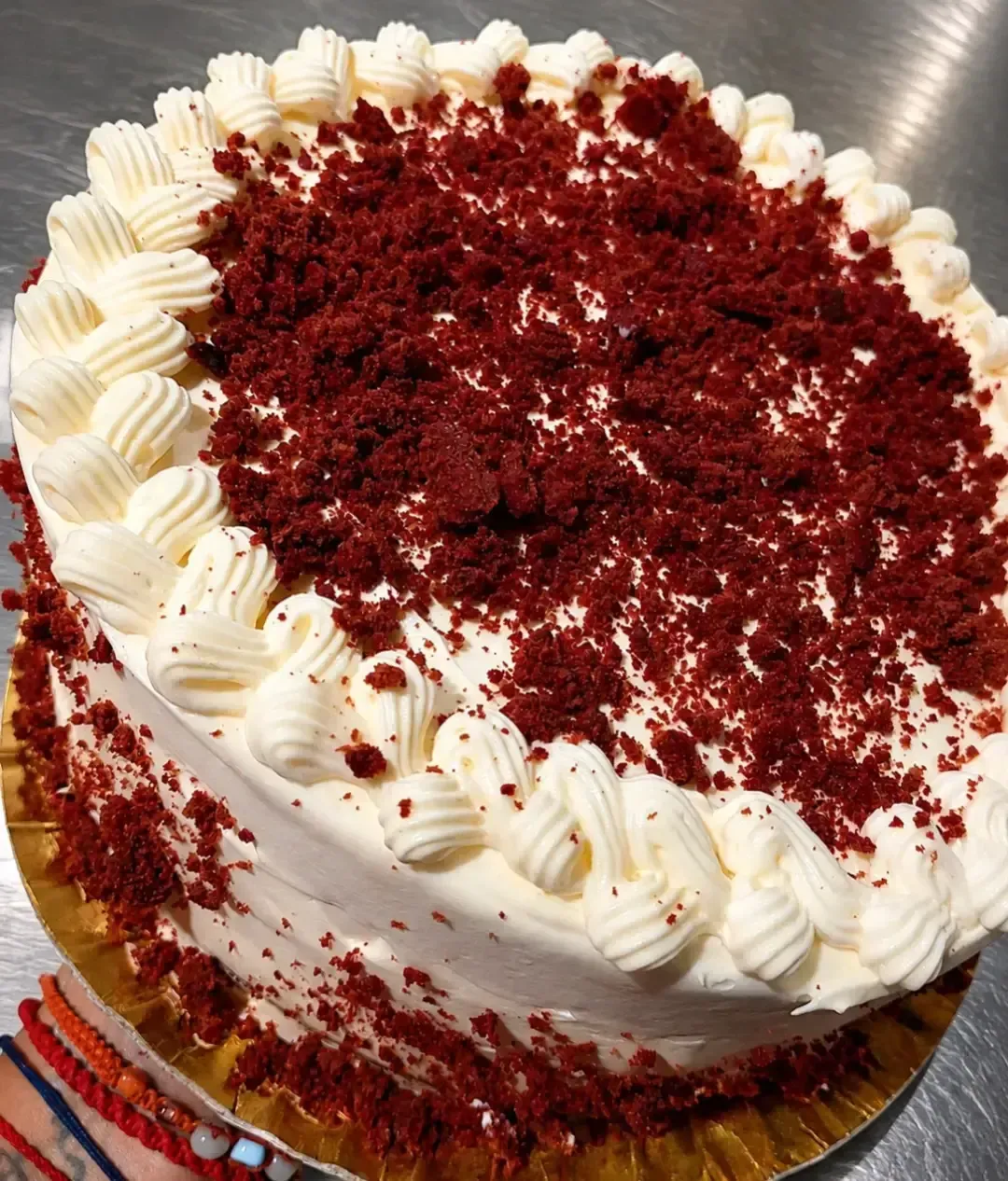 Tarta red velvet con cobertura blanca y migas rojas por encima, sobre una base dorada.