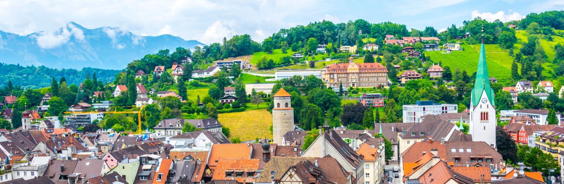 Eine Luftaufnahme einer kleinen Stadt auf einem Hügel mit Bergen im Hintergrund.