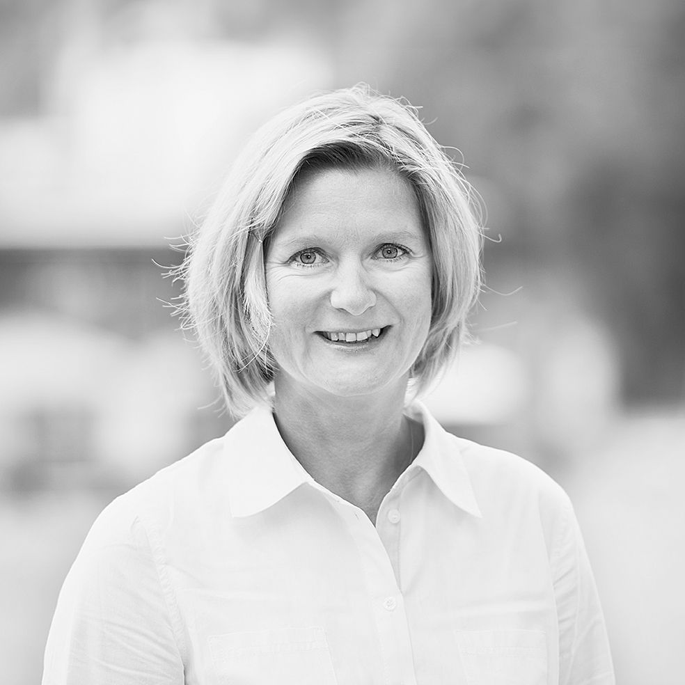 Auf einem Schwarzweißfoto lächelt eine Frau in einem weißen Hemd.