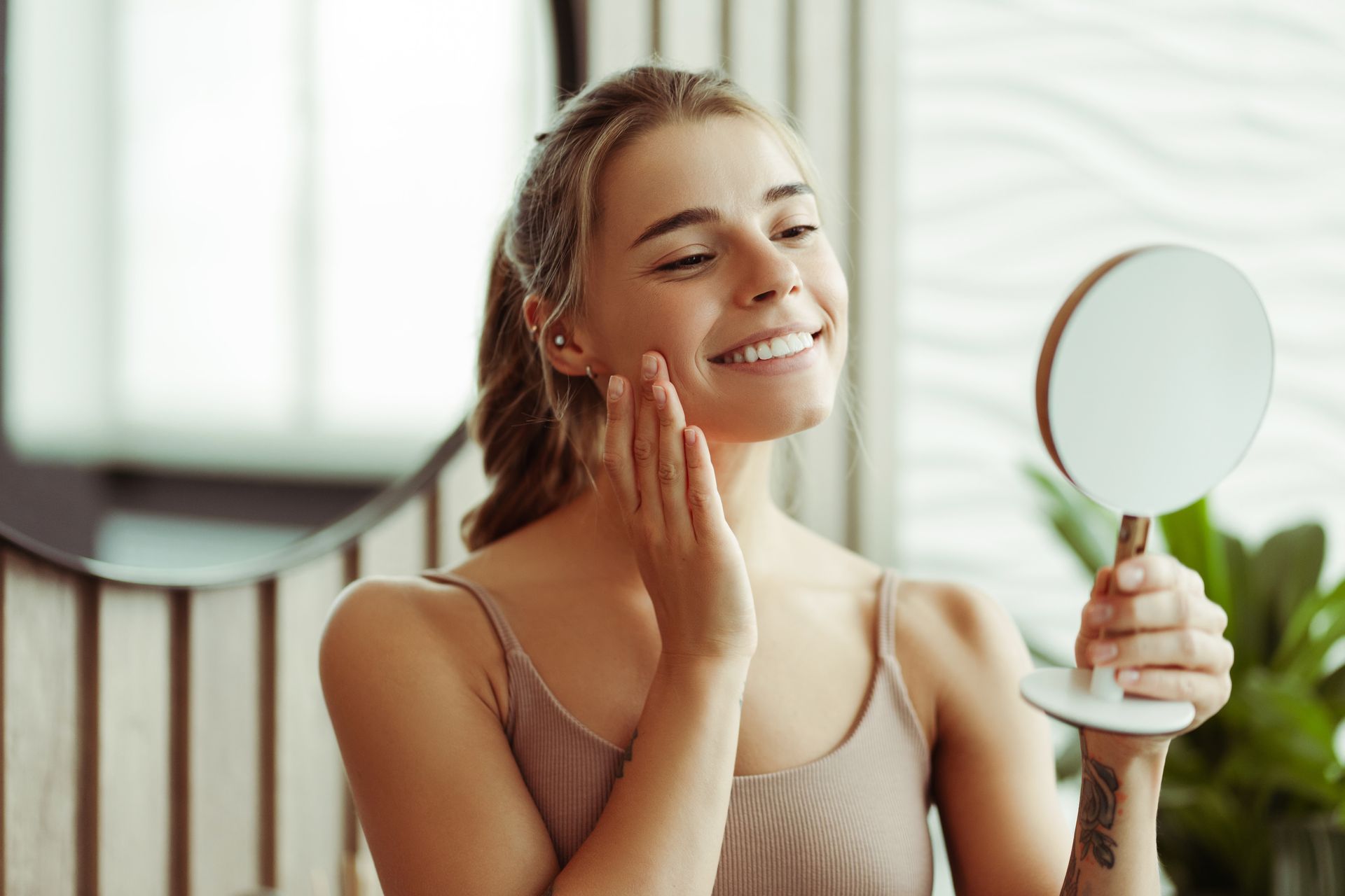 Woman looking at her face while holding a mirror in a bright bathroom