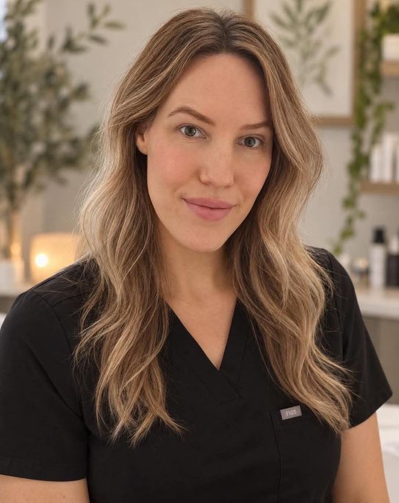 Woman in black top smiling in a softly lit spa or salon setting with plants and candles