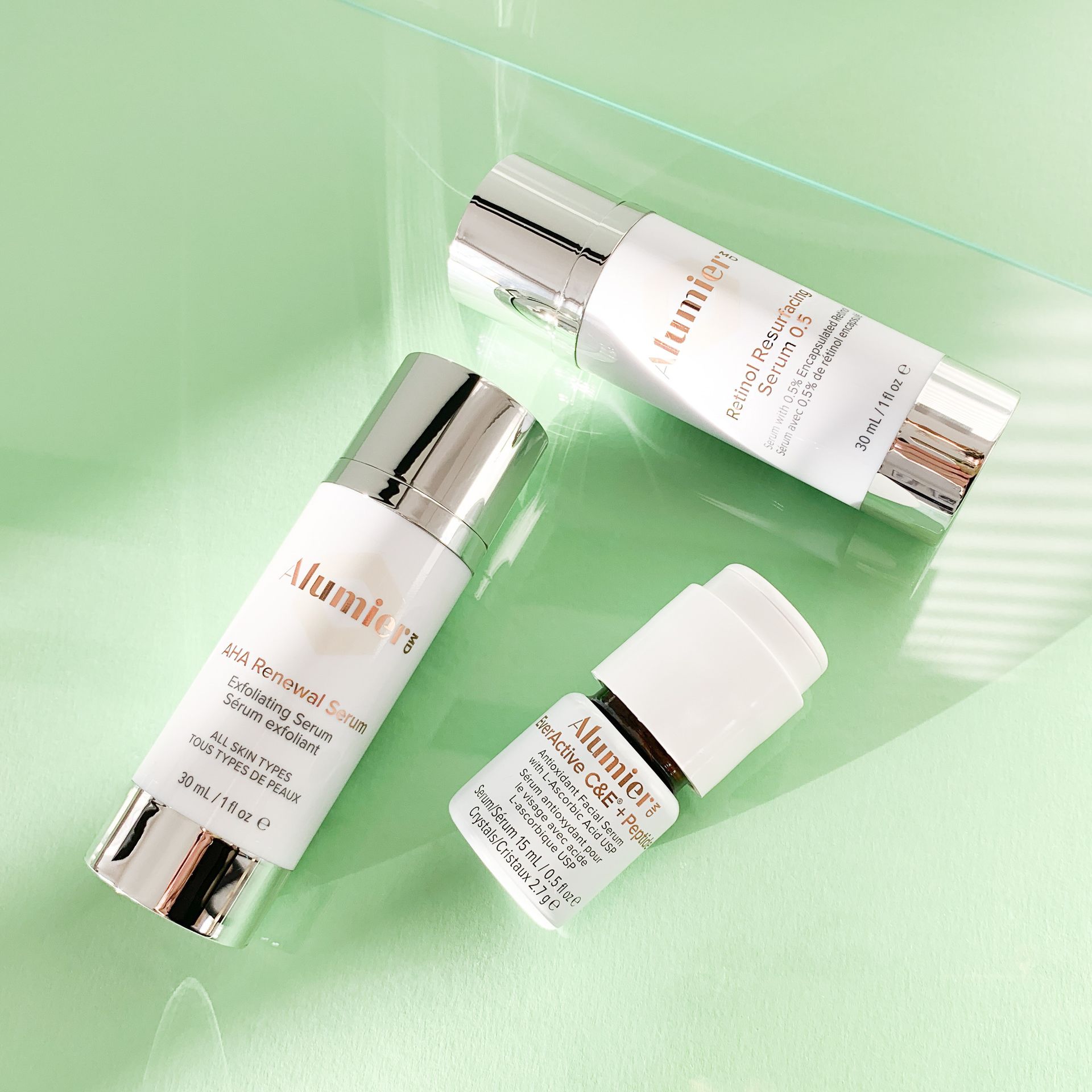 Three white-and-silver skincare bottles on a light green background.