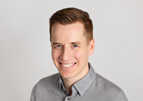 A man in a grey shirt is smiling for the camera.