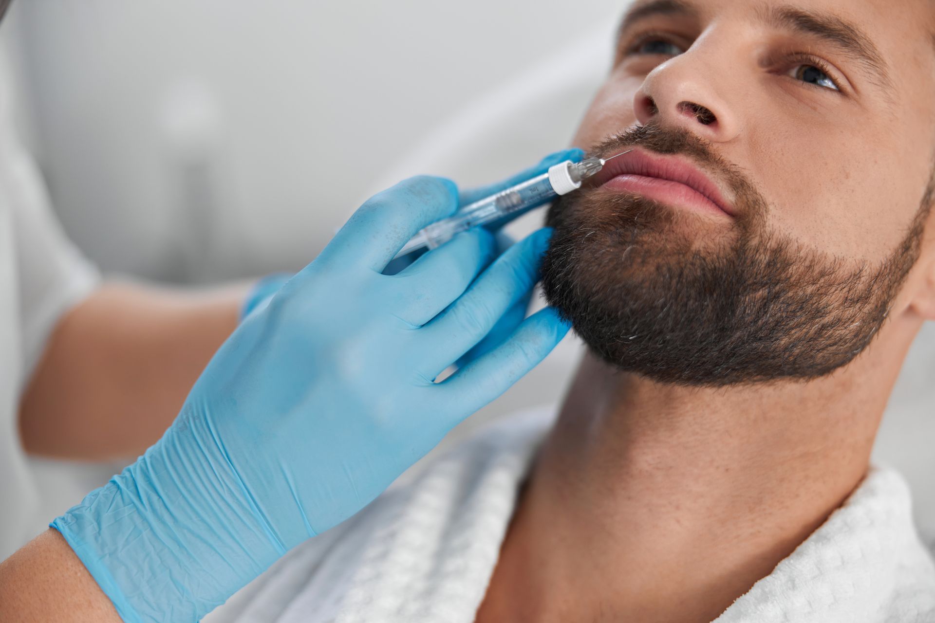 A man with a beard is getting a botox injection in his lips.