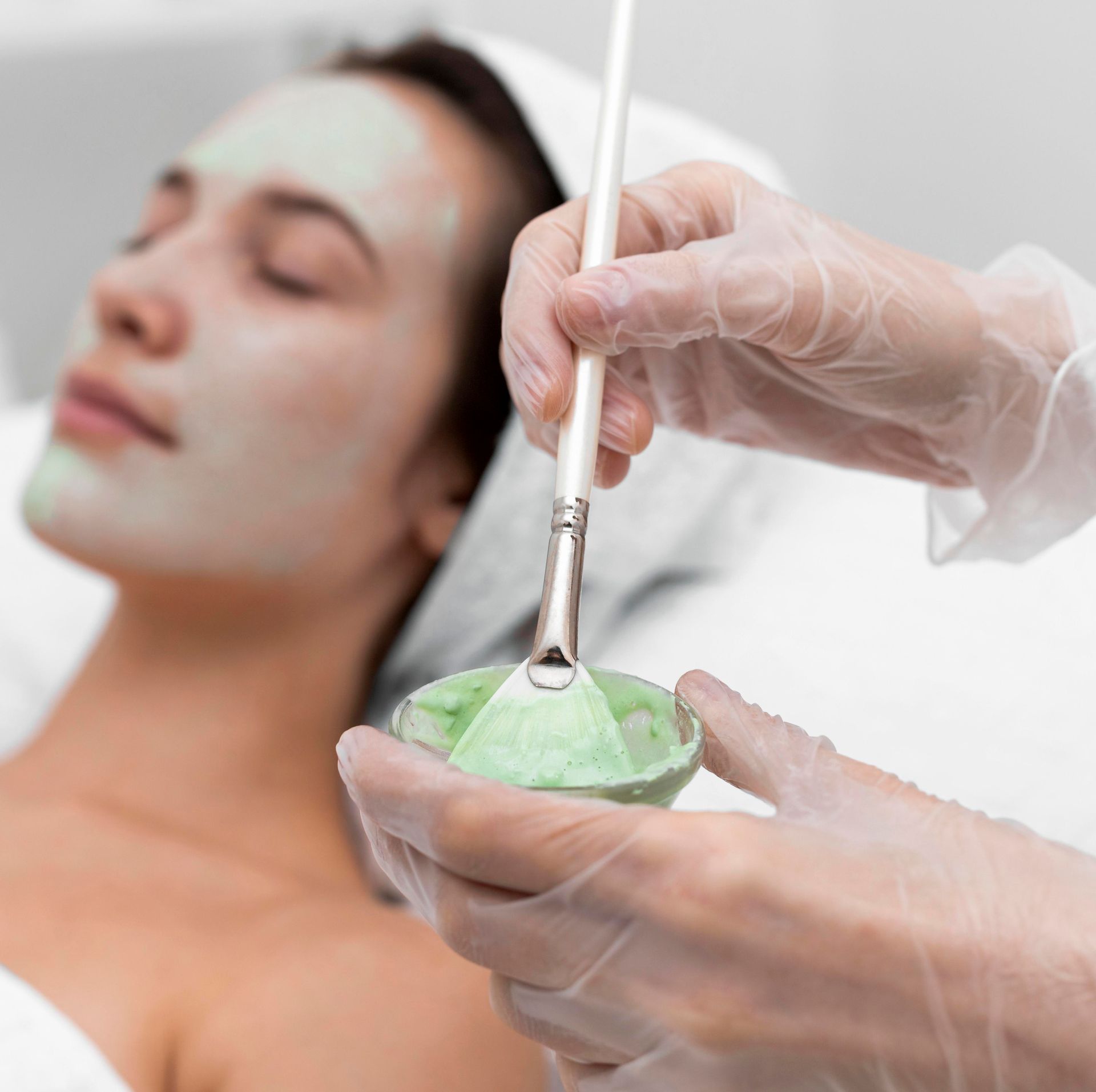 A woman with a green mask on her face is getting a facial treatment.