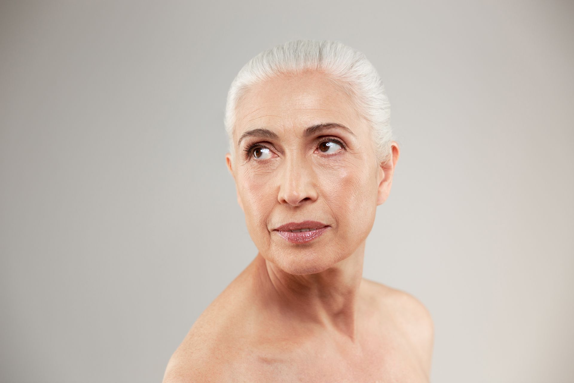 An older woman without a shirt is looking up at the sky.