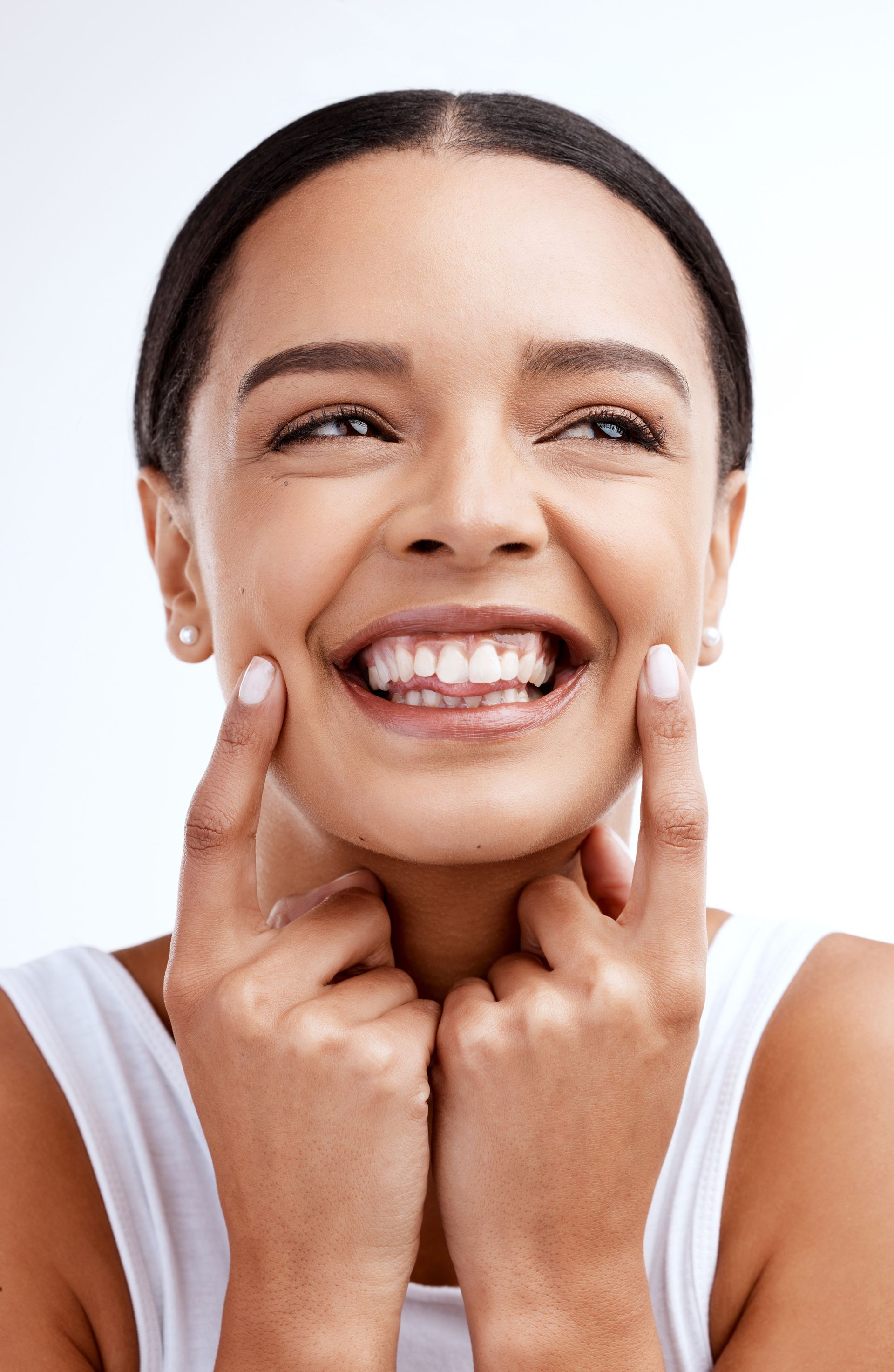 A woman is smiling and touching her face with her fingers.