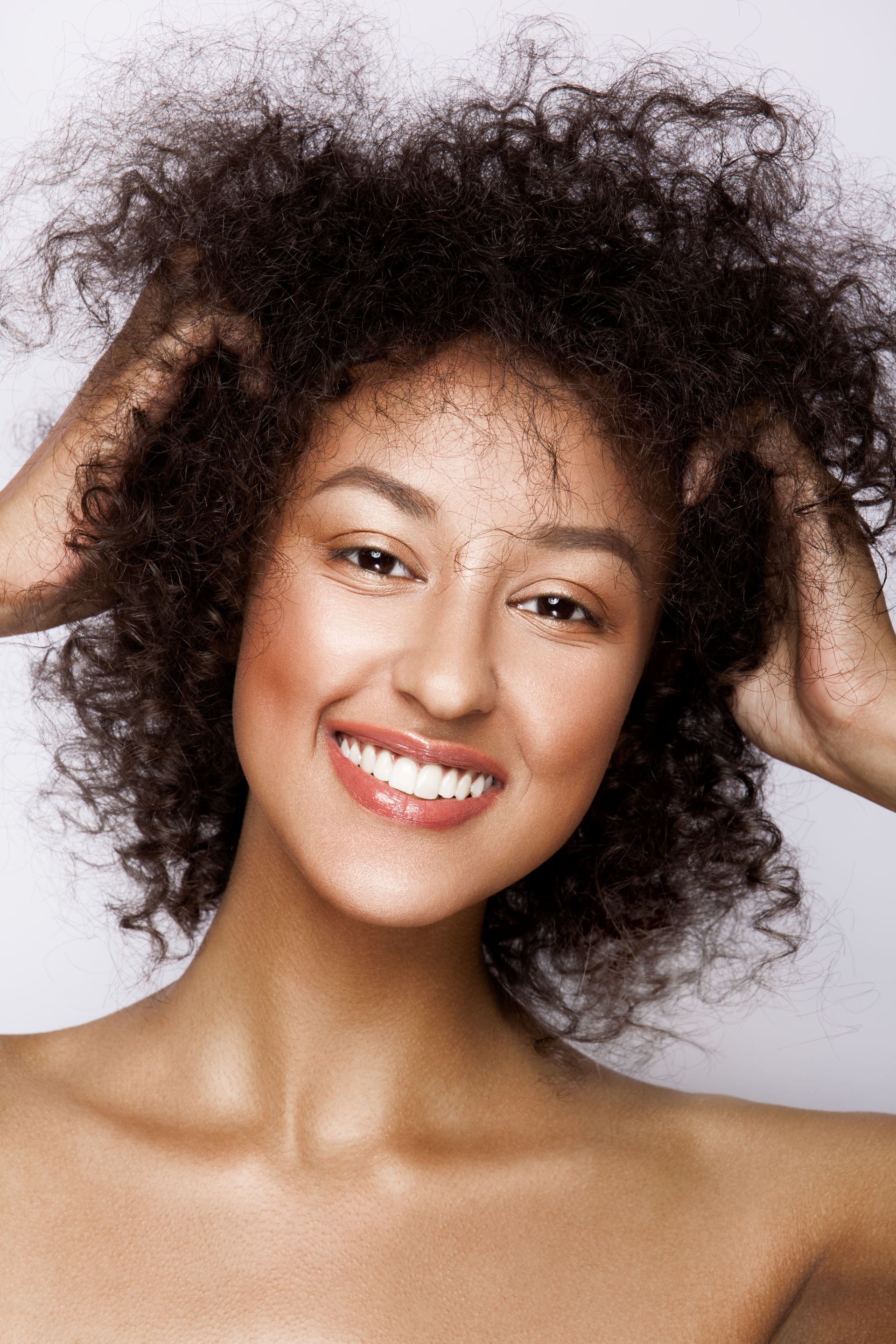 a woman with curly hair is smiling and holding her hair in her hands .