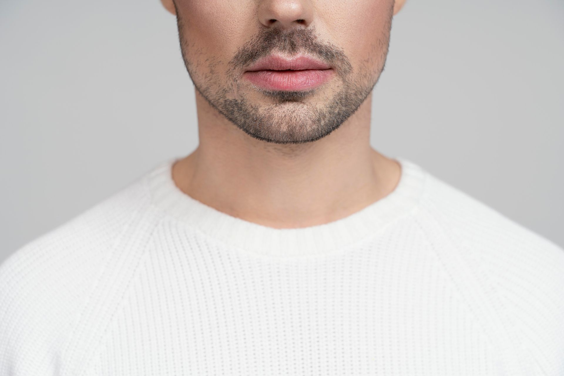 A close up of a man 's face with a beard wearing a white sweater.