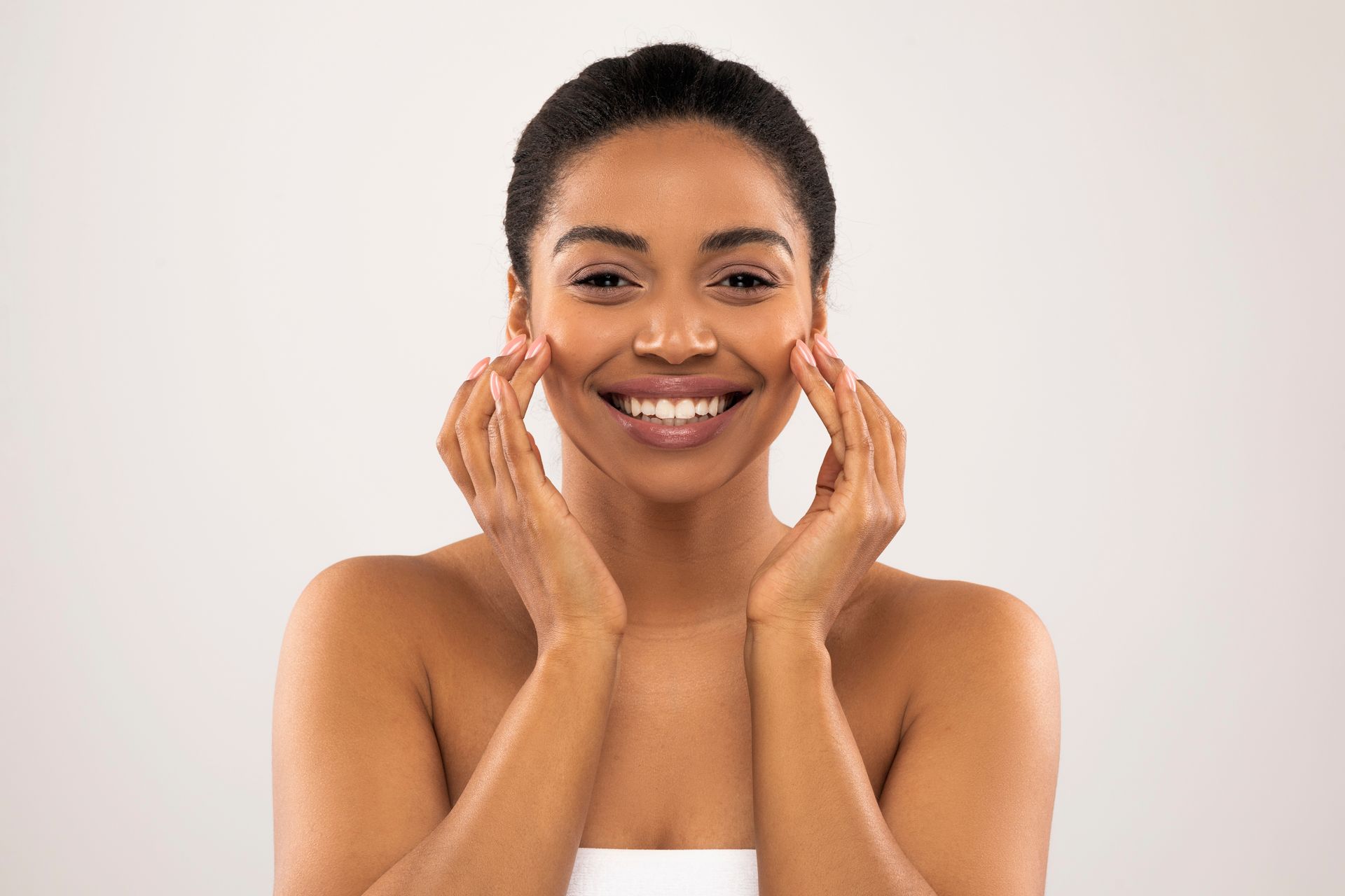 A woman is smiling and touching her face with her hands.