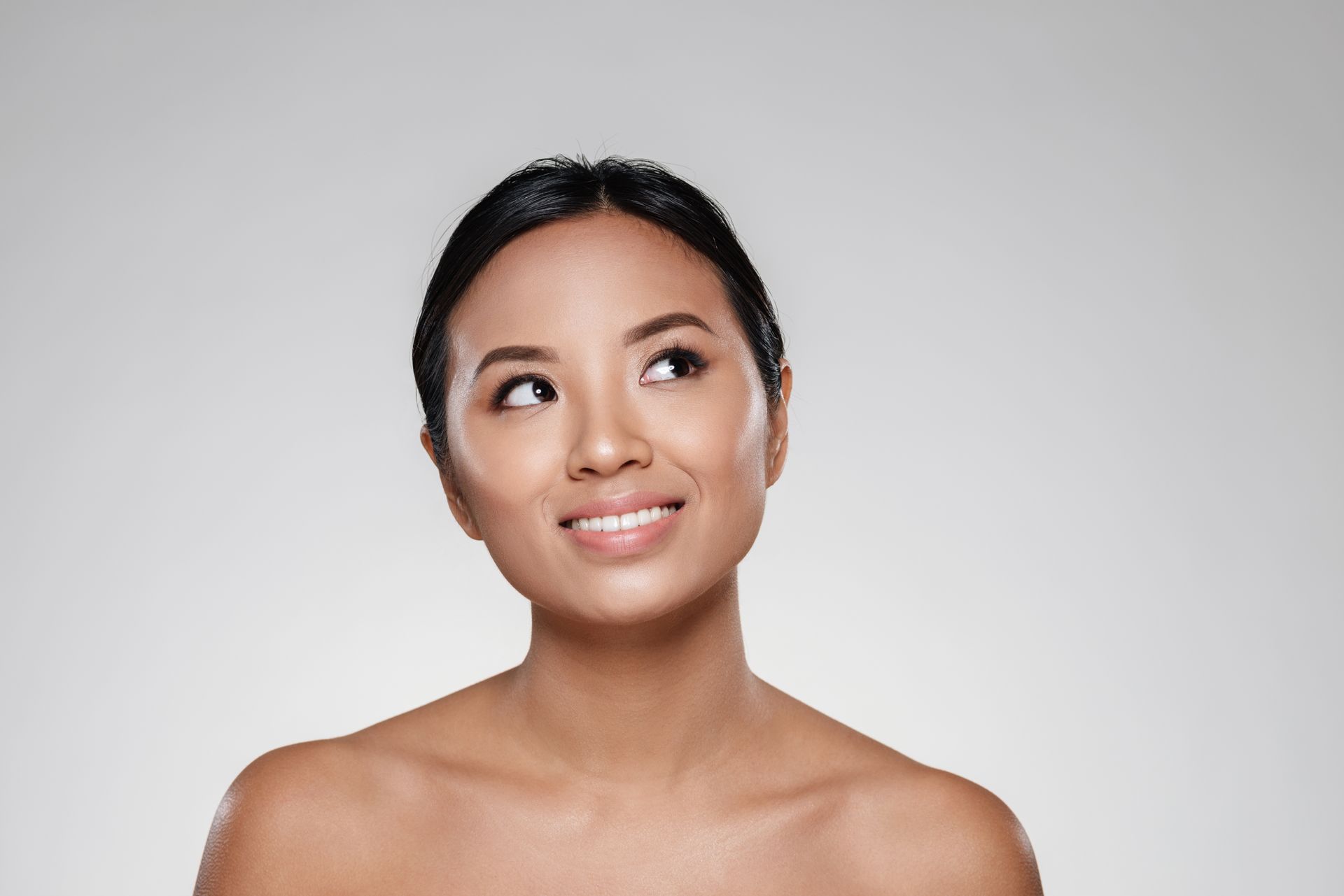 A woman without a shirt is smiling and looking up.