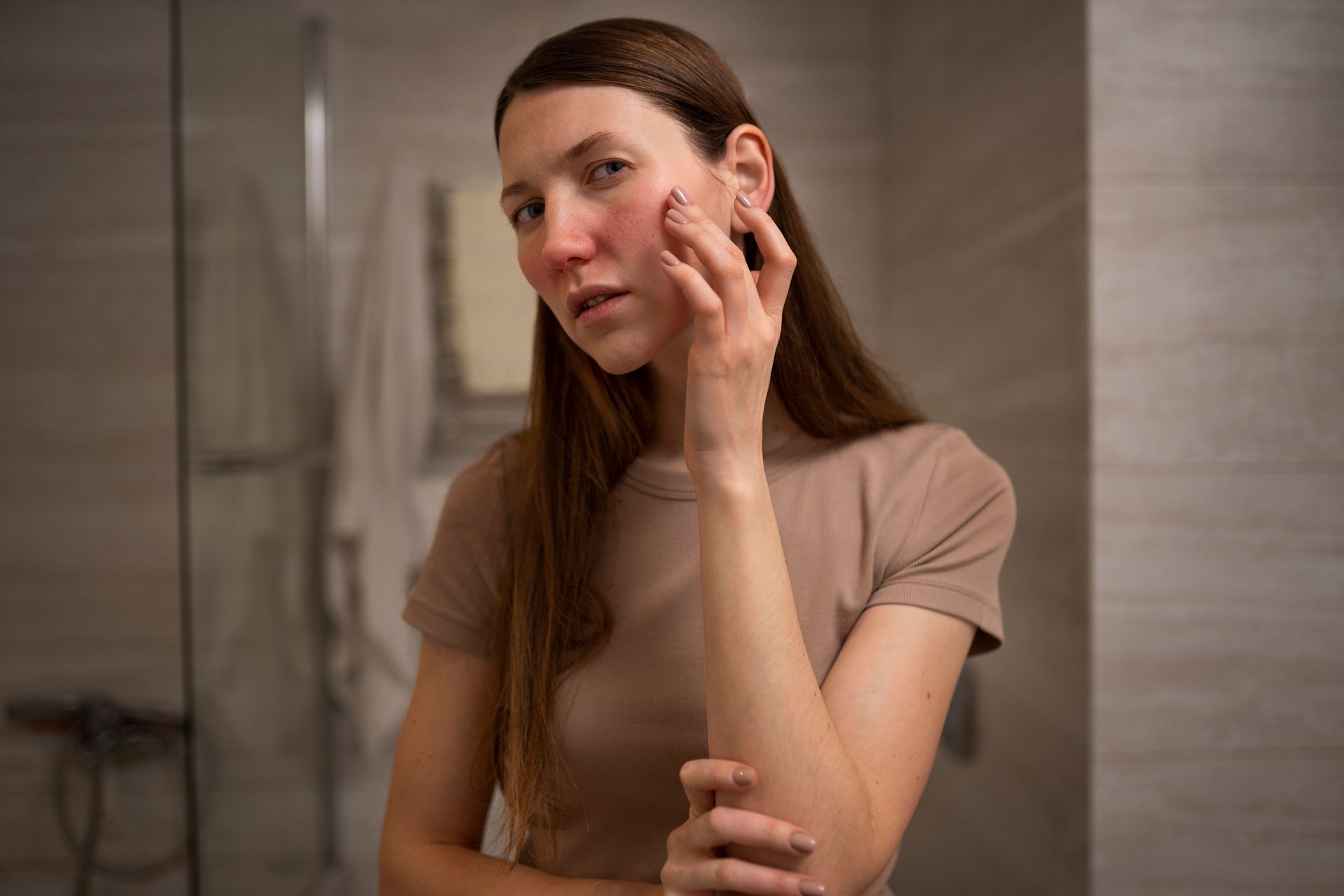 Woman applying skincare cream to her cheek in a bathroom mirror