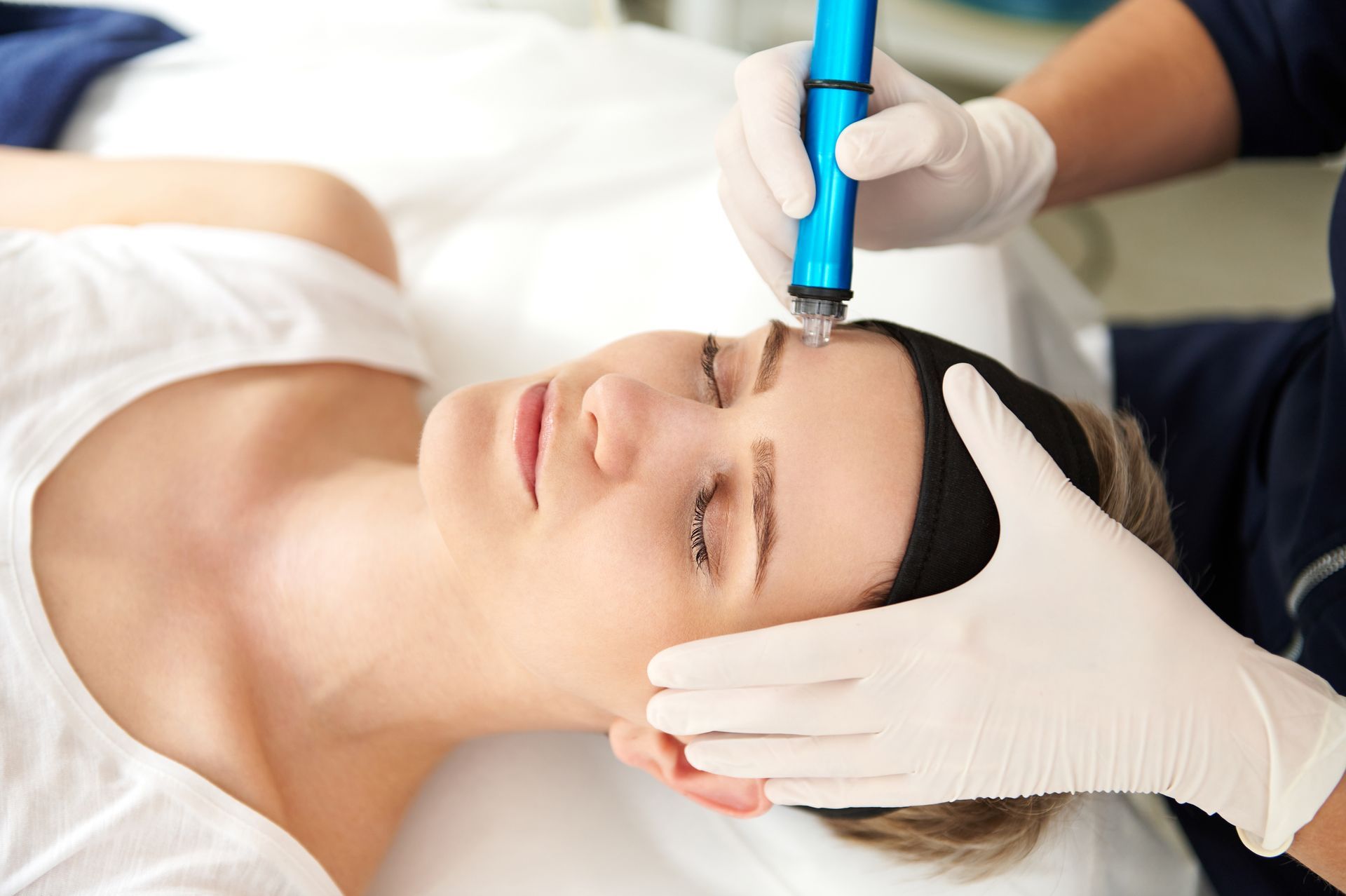Beautician using a blue facial device on a woman lying on a treatment bed