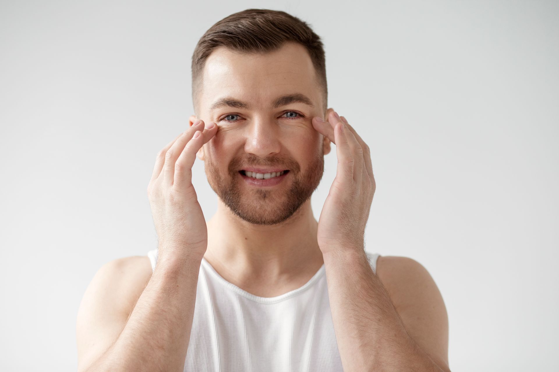 A man is touching his face with his hands and smiling.