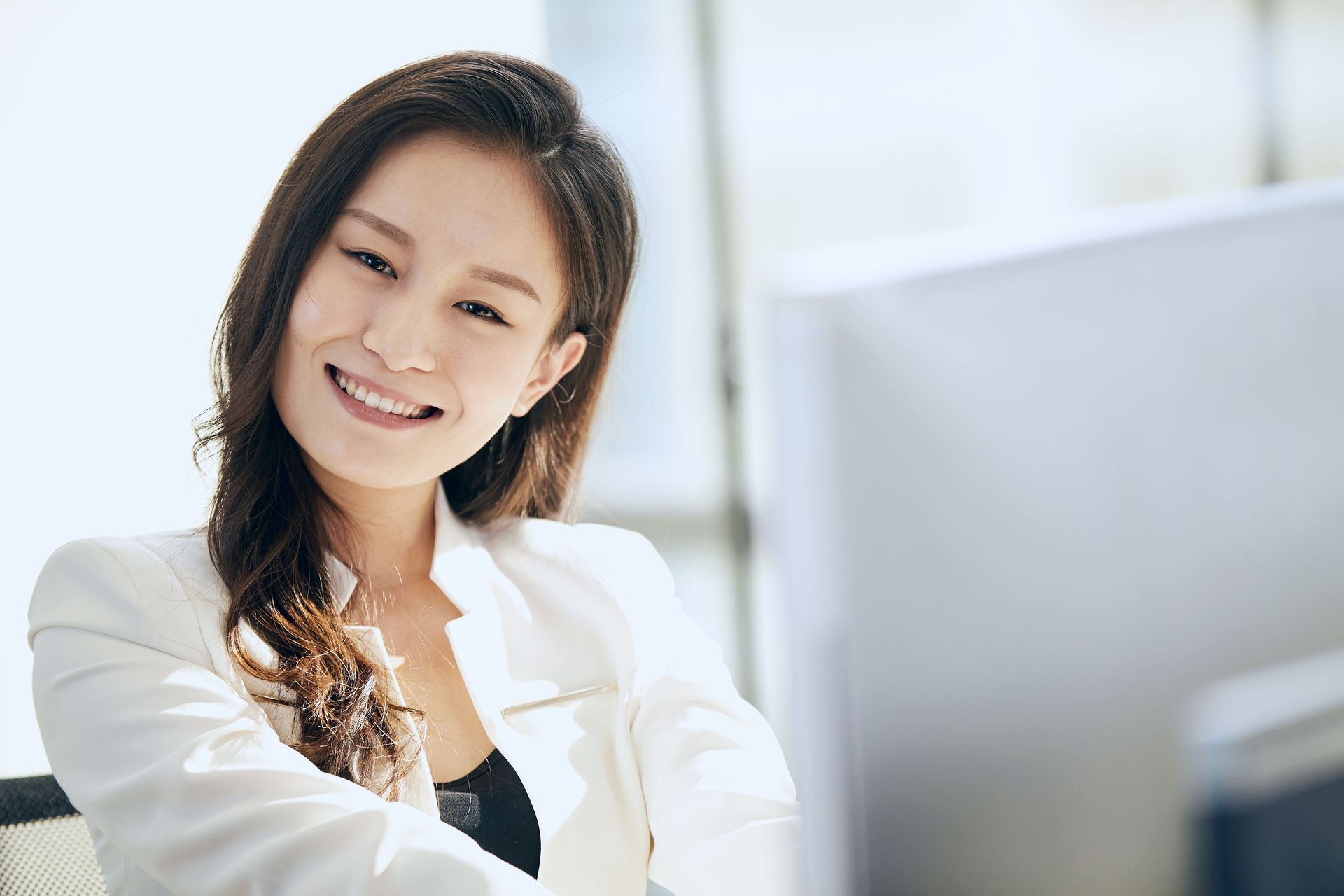 Smiling woman in a white blazer working at a computer in a bright office