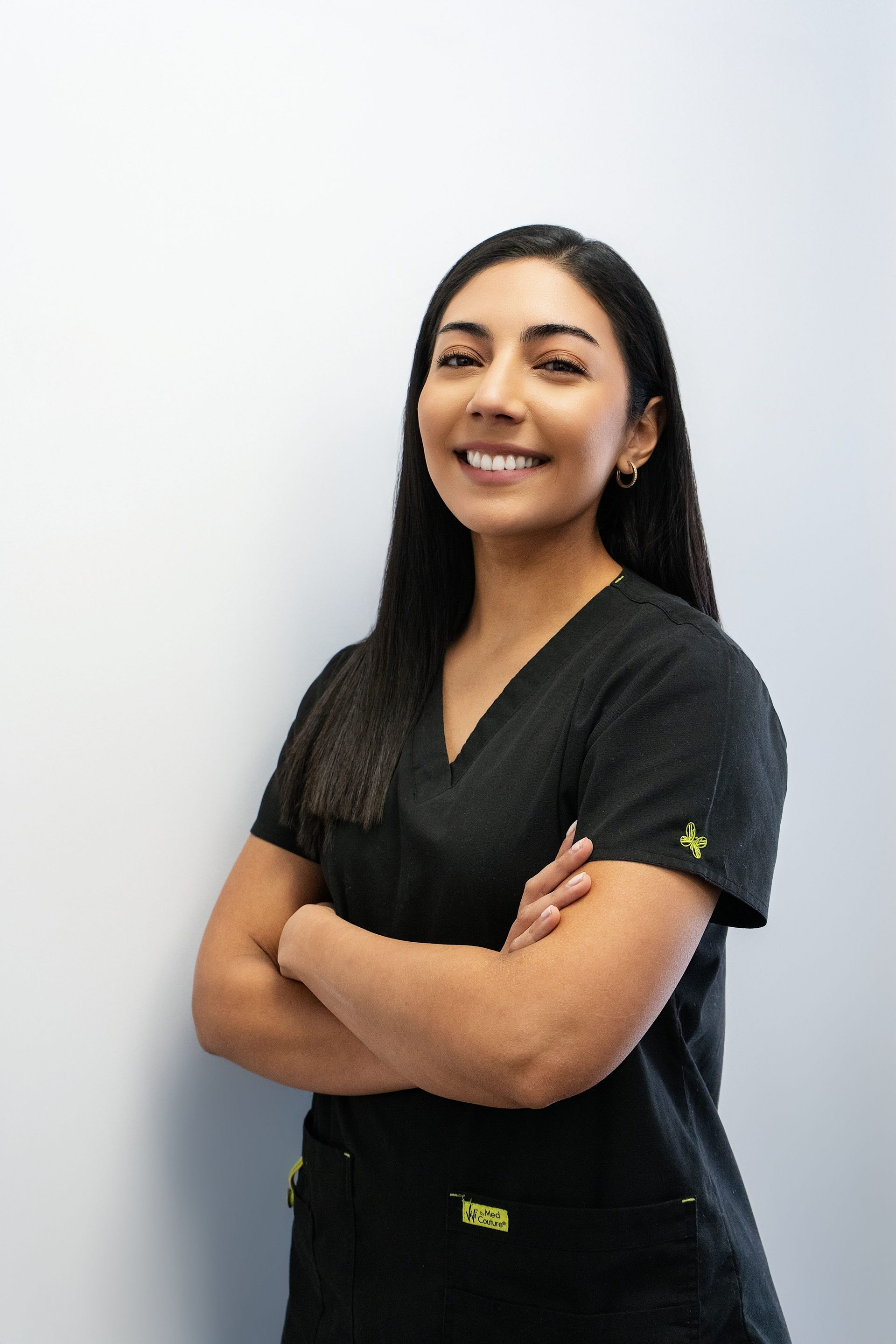 Smiling person in black scrubs standing with arms crossed against a light gray background