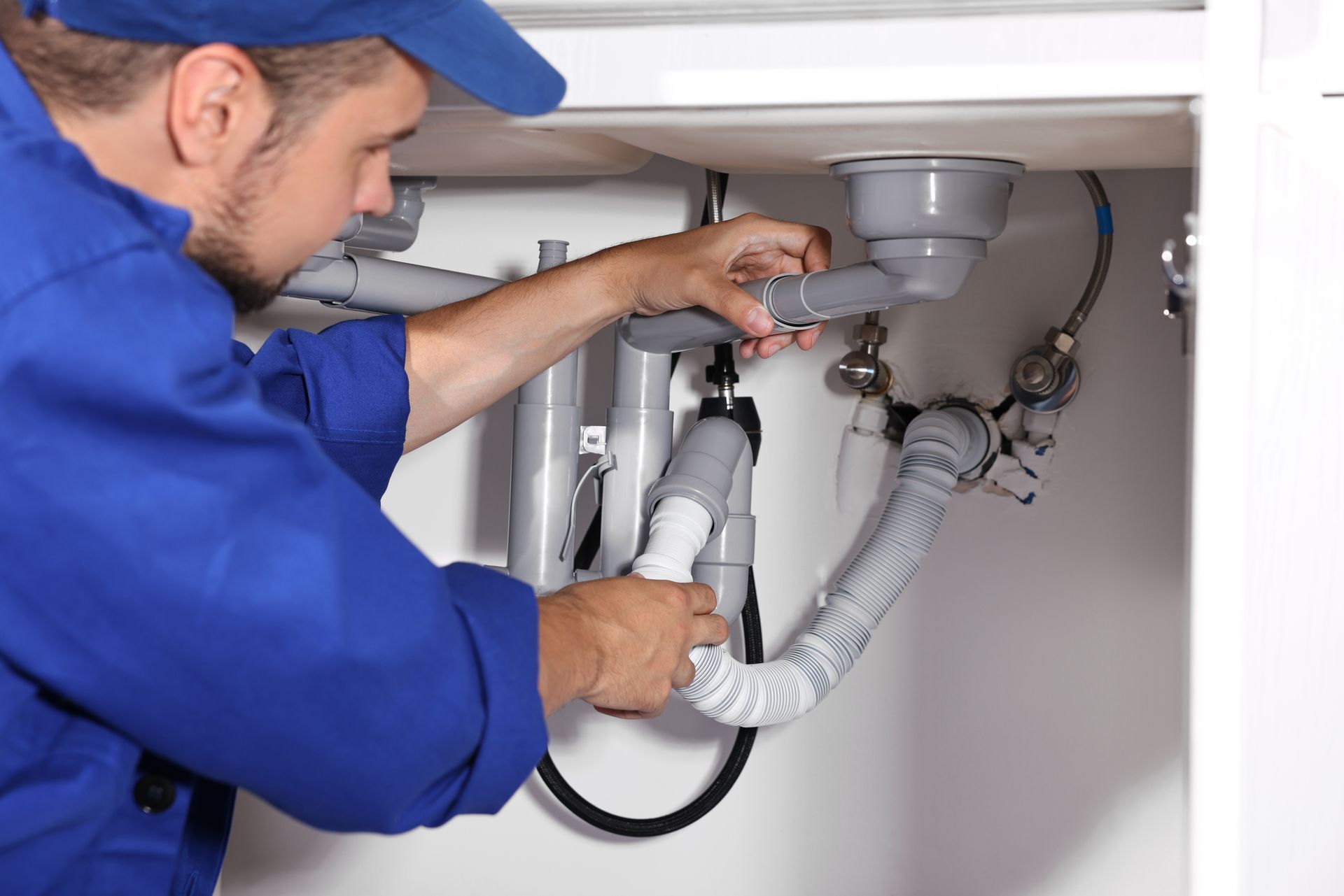 A plumber repairs a pipe under a kitchen sink, tools and plumbing parts around him.