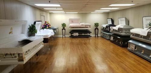 A showroom displaying several open and closed caskets arranged on the floor and pedestals in a brightly lit room.