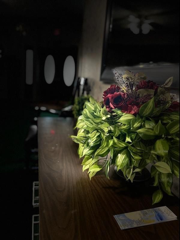 A vibrant bouquet with green leaves and red flowers sits on a dark wooden surface in a dimly lit room.