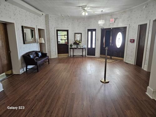 A bright, open foyer with wood-look flooring, light patterned wallpaper, a leather sofa, console table, and double doors.