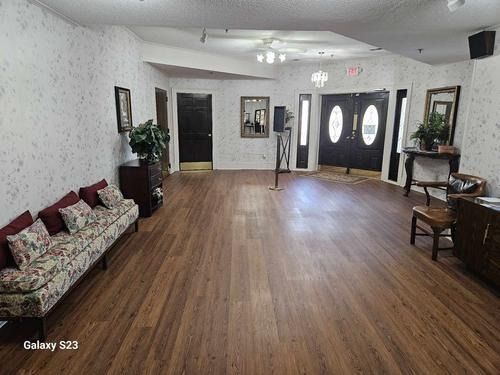 An empty waiting room with floral wallpaper, wood flooring, a long patterned sofa, and double entry doors.